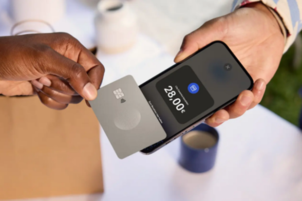 Eine Person hält eine silberne Kreditkarte auf ein Smartphone. Das Display zeigt einen Einkaufsbetrag. © PayPal